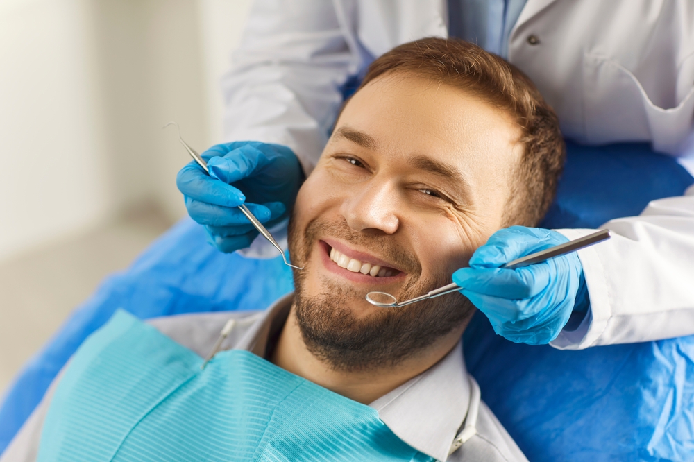 A person in a dentist chair looking nervous as a dentist, the "doctor of the mouth", leans over them with a dental tool. The dentist is wearing a mask and protective eyewear, and the dental office appears clean and modern. No text on image.